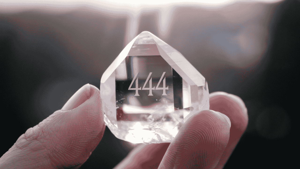 Hand holding a crystal with the number 444 engraved, symbolizing spiritual energy and manifestation.